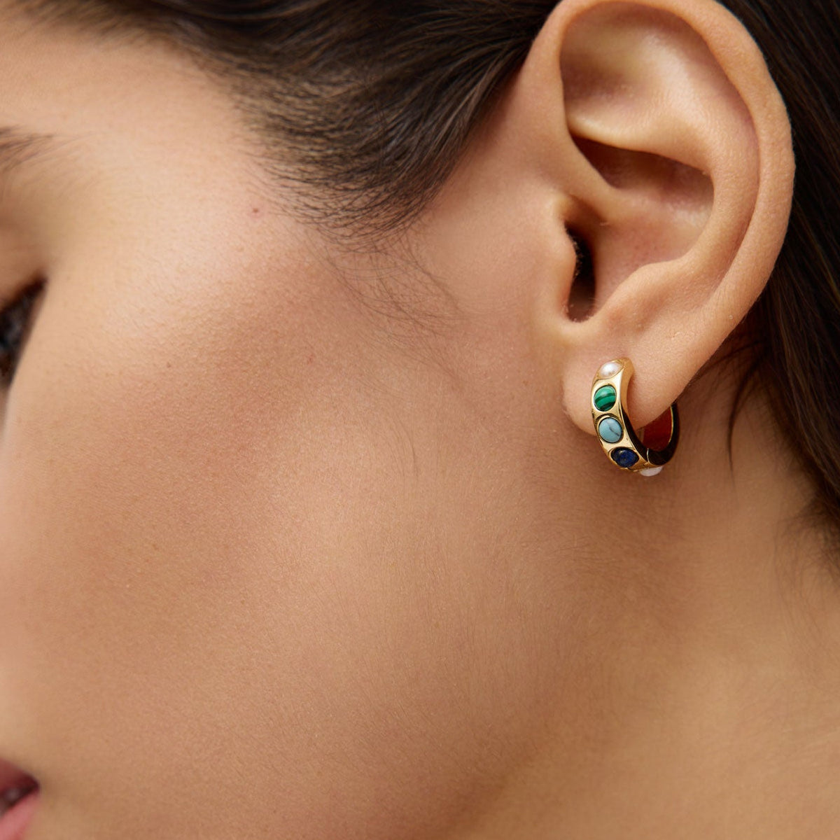 Close-up of a woman's ear wearing a colorful stone hoop earring.
