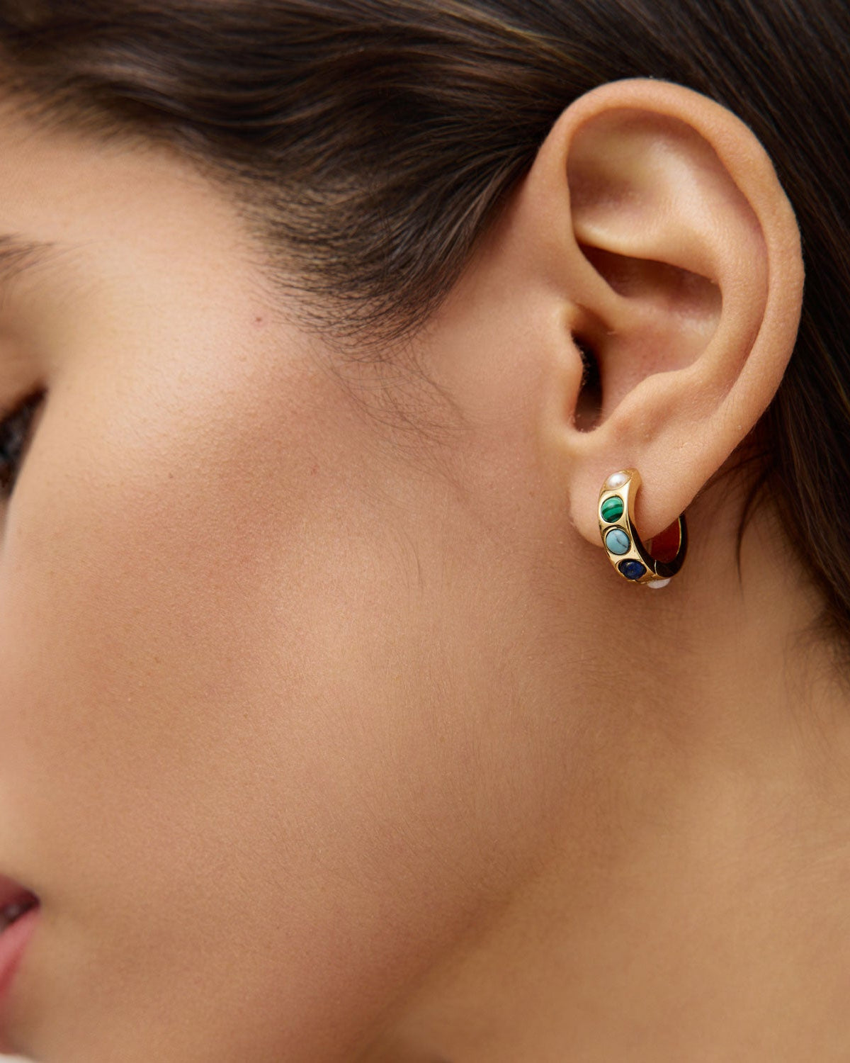 Close-up of a woman's ear wearing a colorful stone hoop earring.