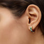 Close-up of a woman's ear wearing a colorful stone hoop earring.