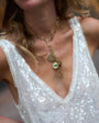 Close-up of a person wearing a gold necklace with charms on a sequined top.