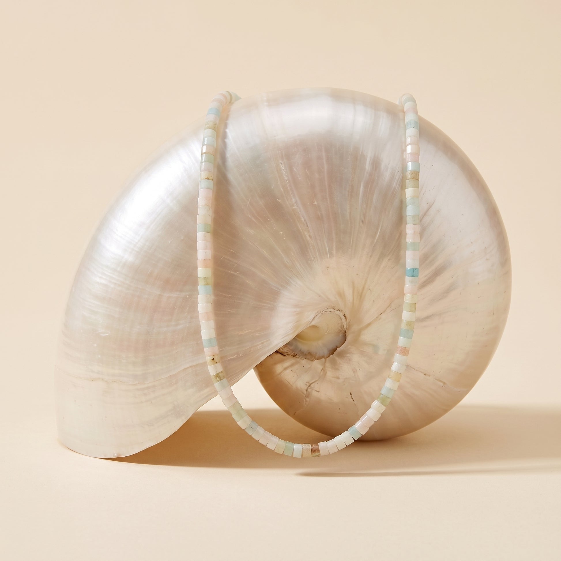 A shell-shaped decorative object draped with two beaded necklaces on a warm beige studio background.