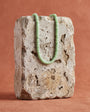A light green beaded necklace draped over a rough, textured stone block against a warm terracotta background.