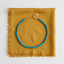 A turquoise beaded necklace with a gold clasp, displayed on a folded mustard yellow fabric with fringe, shot against a clean white background.