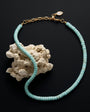 A turquoise beaded necklace with a gold chain clasp, displayed on a textured white rock against a solid black background.