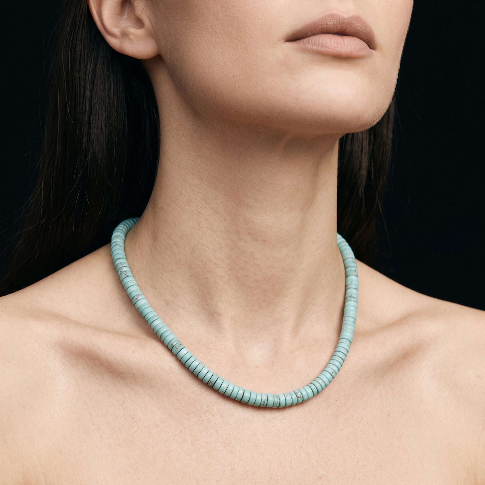A close-up of a model wearing a light blue-green beaded necklace against a dark background.