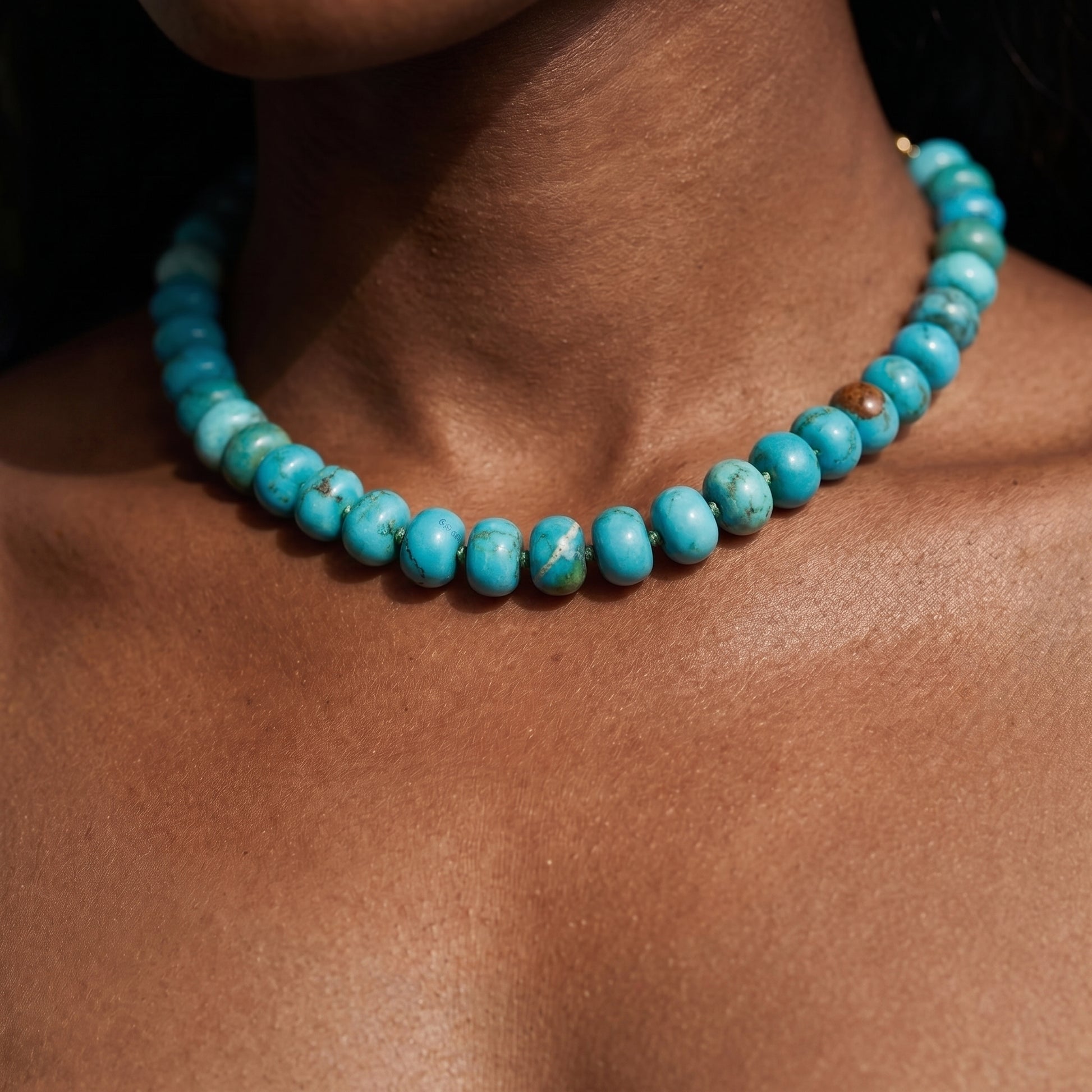 A close-up of a person wearing a turquoise beaded necklace, showing the beads against the skin.