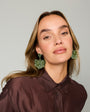 Model wearing green embroidered and beaded statement earrings against a white background
