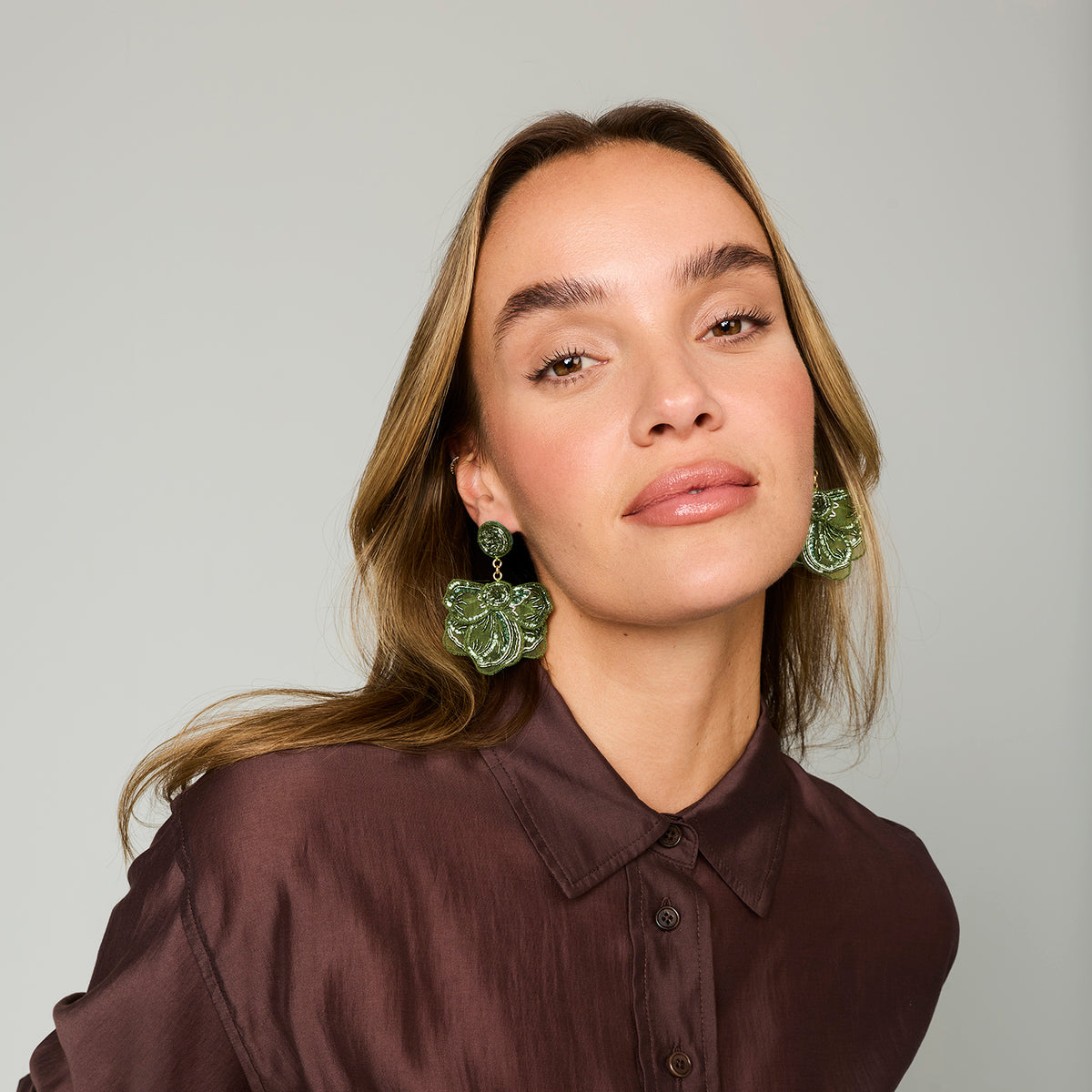 Model wearing green embroidered and beaded statement earrings against a white background