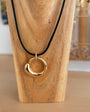 A gold crescent-shaped pendant necklace on a black cord, displayed on a wooden stand.
