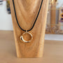 A gold crescent-shaped pendant necklace on a black cord, displayed on a wooden stand.