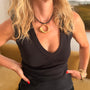 A close-up lifestyle shot of a woman wearing a black V-neck tank top and a black cord necklace with a chunky gold ring pendant. She has blonde hair and is wearing gold bracelets on her wrist.