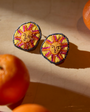 Embroidered earrings with faces surrounded by oranges on marble background