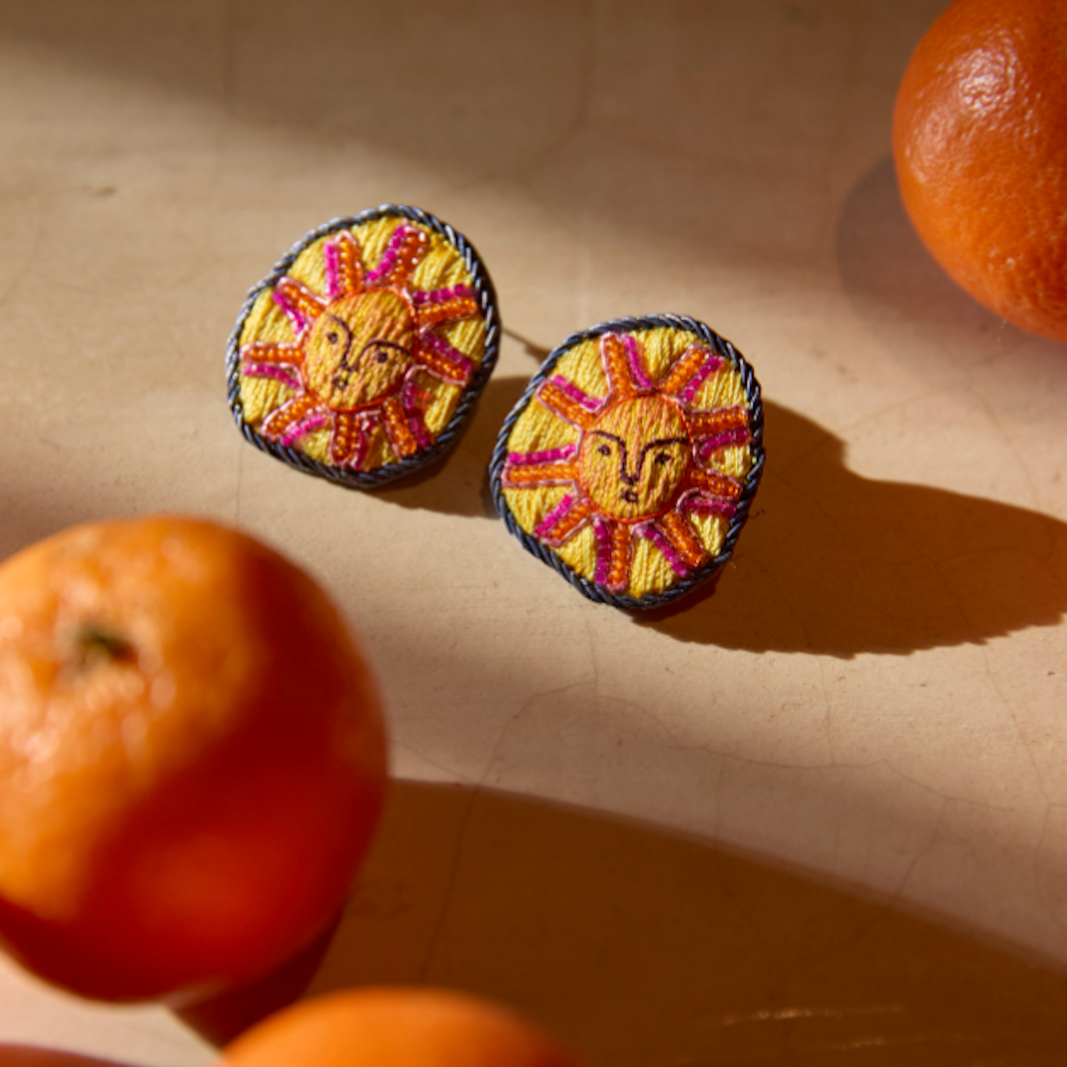 Embroidered earrings with faces surrounded by oranges on marble background