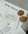 Two sun-shaped earrings on a piece of paper with 'Hotel Sevilla' printed on it.