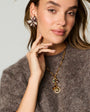 Model wearing floral embroidered earrings and a charm and chain necklace with a sweater