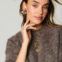 Model wearing floral embroidered earrings and a charm and chain necklace with a sweater