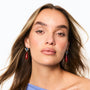 A close-up portrait of a woman with long brown hair wearing dangling earrings with red teardrop charms and silver-toned tops, against a plain white background.