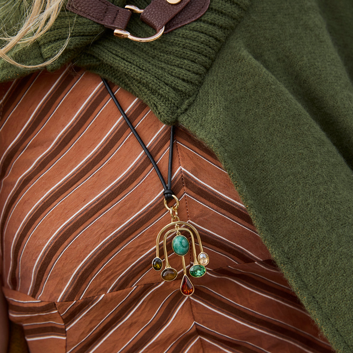 Model wearing a gold crescent moon pendant necklace with green and brown beads on a black cord, in a green sweatr jacket
