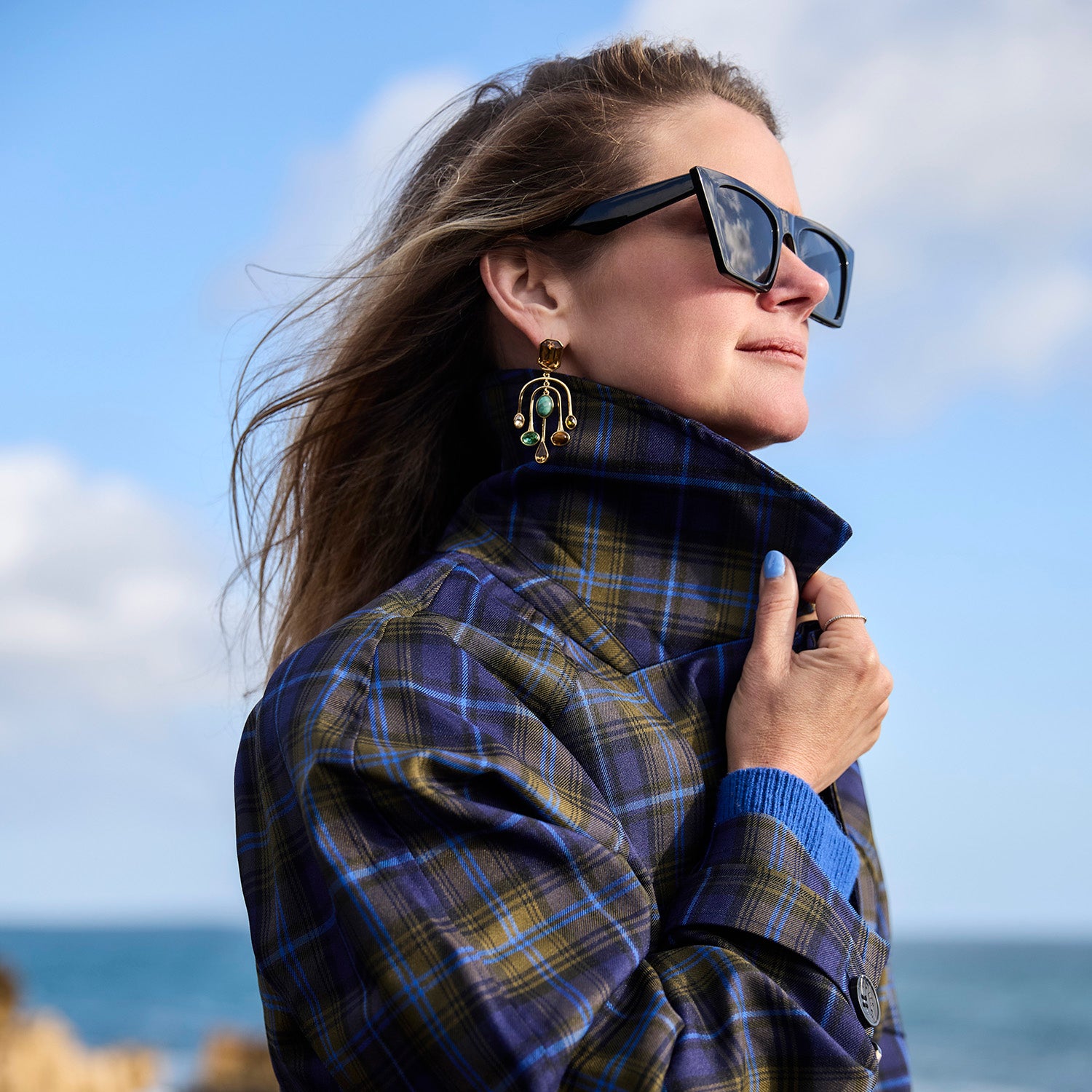 Model wearing chandelier style drop earrings with semi precious stones and gemstones against a beach backgrouond