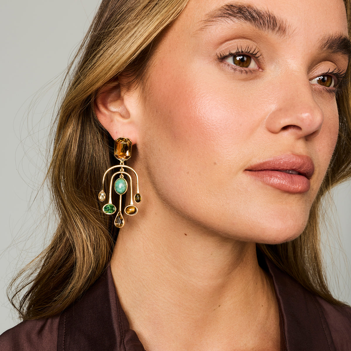 Model wearing chandelier style drop earrings with semi precious stones and gemstones against a whit background