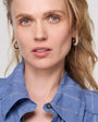 Woman wearing a blue shirt with pearl earrings against a plain background