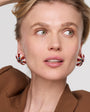 Woman wearing a brown outfit with colorful embroidered and beaded earrings on a plain background