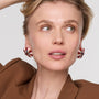 Woman wearing a brown outfit with colorful embroidered and beaded earrings on a plain background
