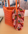 Orange woven handbag with a colorful scarf draped over it on a wooden surface.