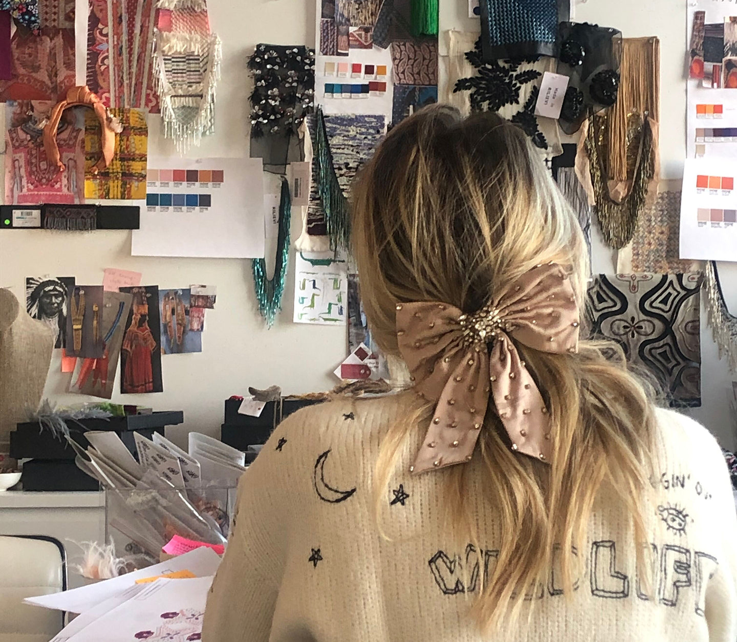 Person with a decorative bow in their hair in an office setting with colorful materials on the wall.