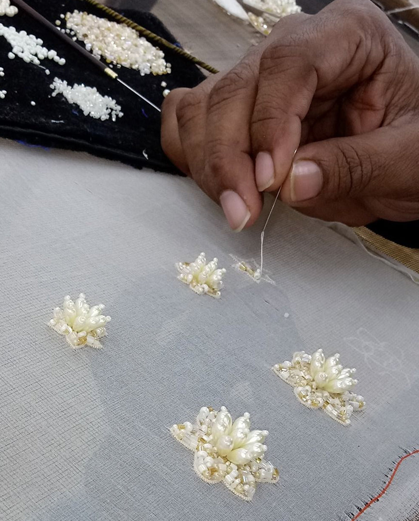 Person working on embroidery with pearl-like beads on fabric