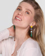 Model wearing colorful drop earrings on white background.