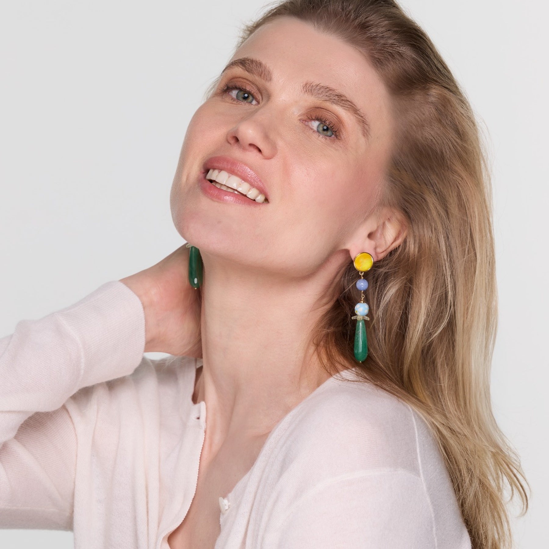 Model wearing colorful drop earrings on white background.