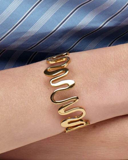 Gold spiral cuff on a person's wrist with a blue striped fabric background