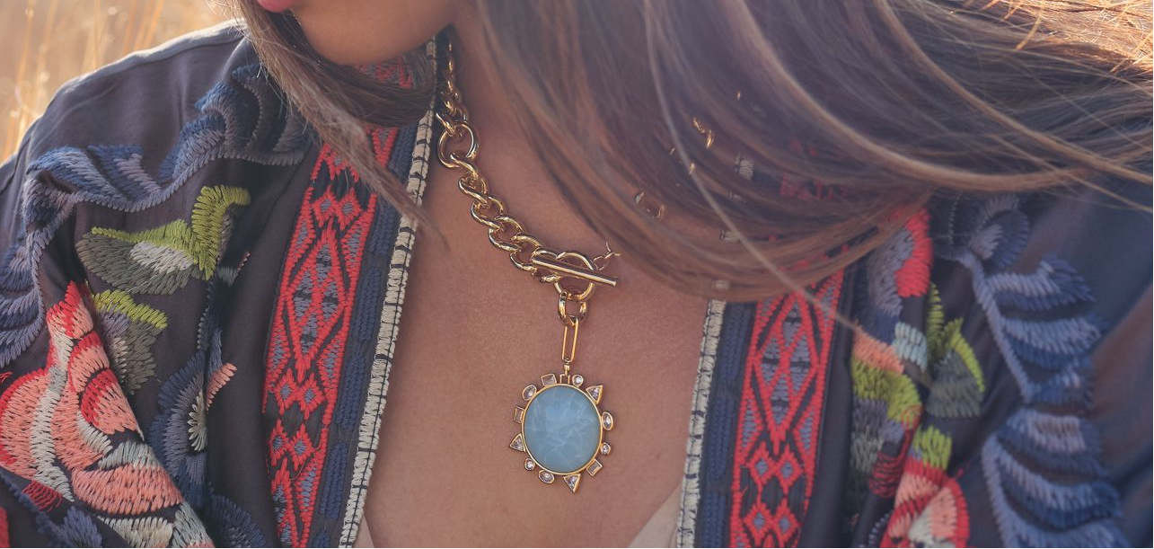 Person wearing a patterned top with a necklace featuring a blue pendant.
