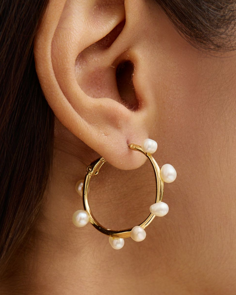 Woman wearing a gold hoop earring with pearls and a beaded necklace.