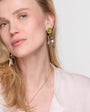 Woman wearing gold earrings with green gemstones on a white background
