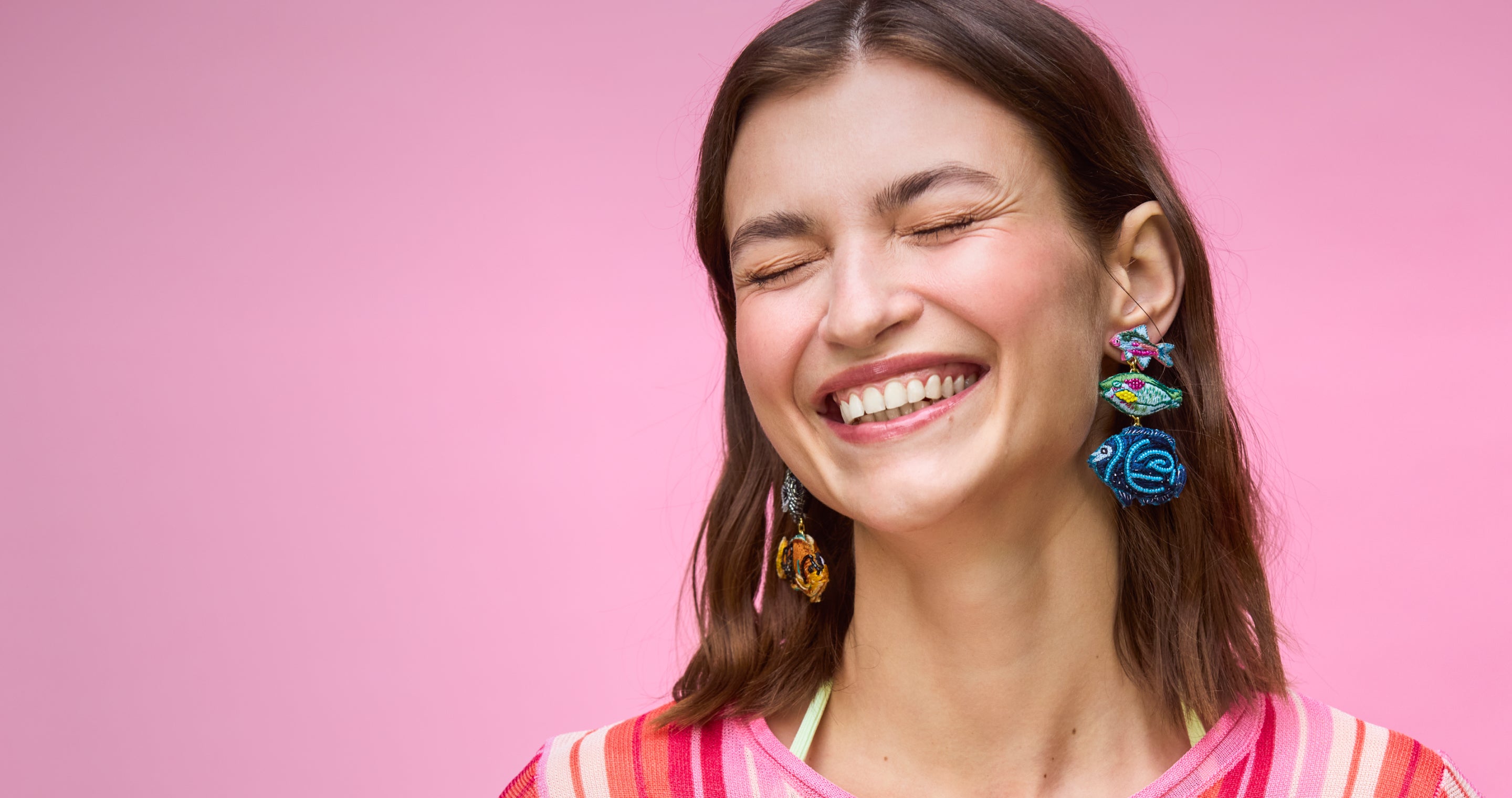 Model wearing fish shaped earrings against a pink background while smiling