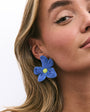 Close-up of a woman wearing blue flower-shaped earrings on a white background