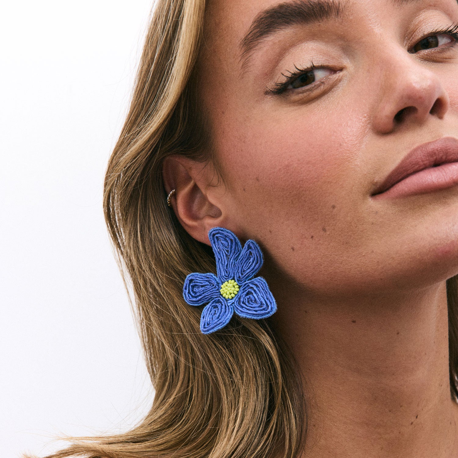 Close-up of a woman wearing blue flower-shaped earrings on a white background