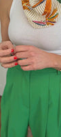Model wearing green pants and white tank top showing off a gold squiggle-like bracelet