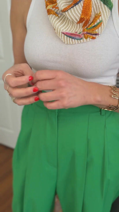 Model wearing green pants and white tank top showing off a gold squiggle-like bracelet