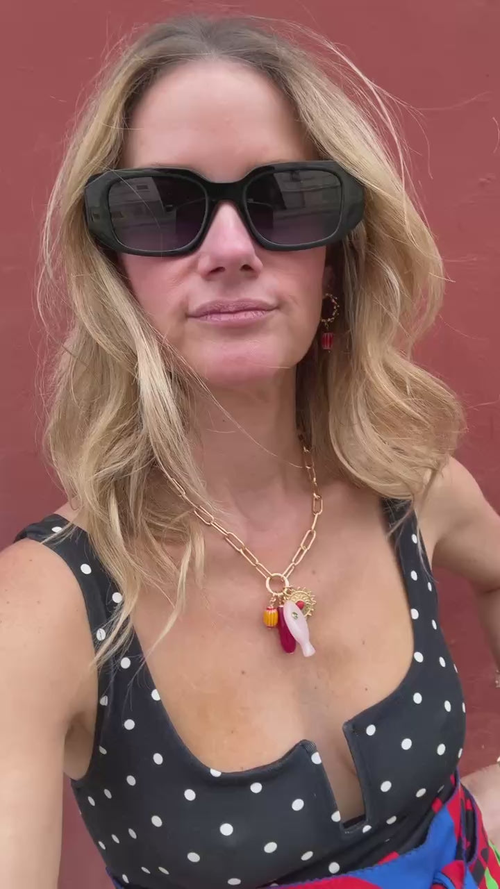 Model wearing gold hoop earrings and gold charm necklace with fish and shell shaped charms against red background