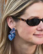 Model wearing beaded and embroidered butterfly earrings with sunglasses on her face against a wooden door