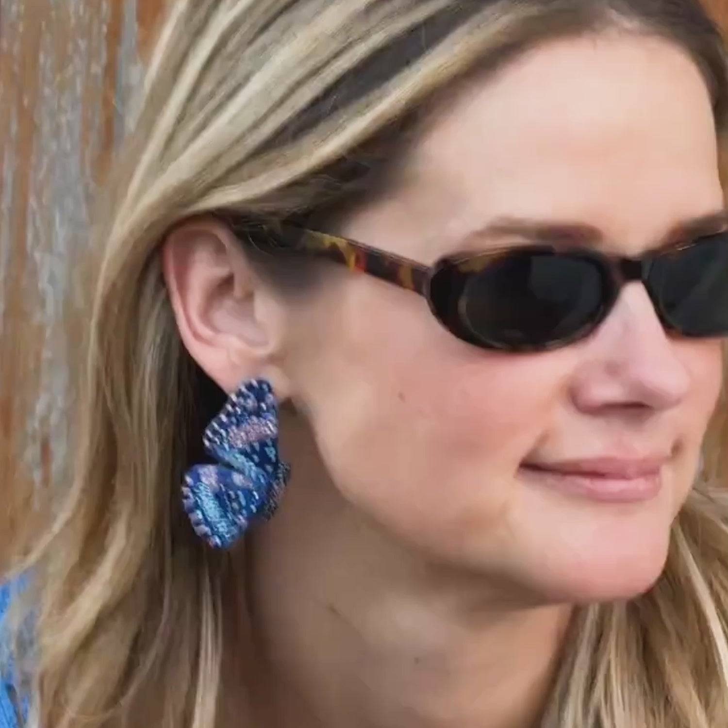 Model wearing beaded and embroidered butterfly earrings with sunglasses on her face against a wooden door