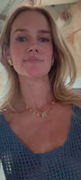 Model wearing colorful gemstone charm necklace and gold and crystal stud earrings wearing a blue dress against a stone background