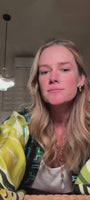 Model showing off gold palm tree shaped stud earring with a long gold chain necklace with a pearl pendant wearing a multicolor robe