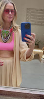 Model wearing peach cover up set with pink swimsuit tying a colorful embroidered and beaded scarf necklace around neck with sunglasses on