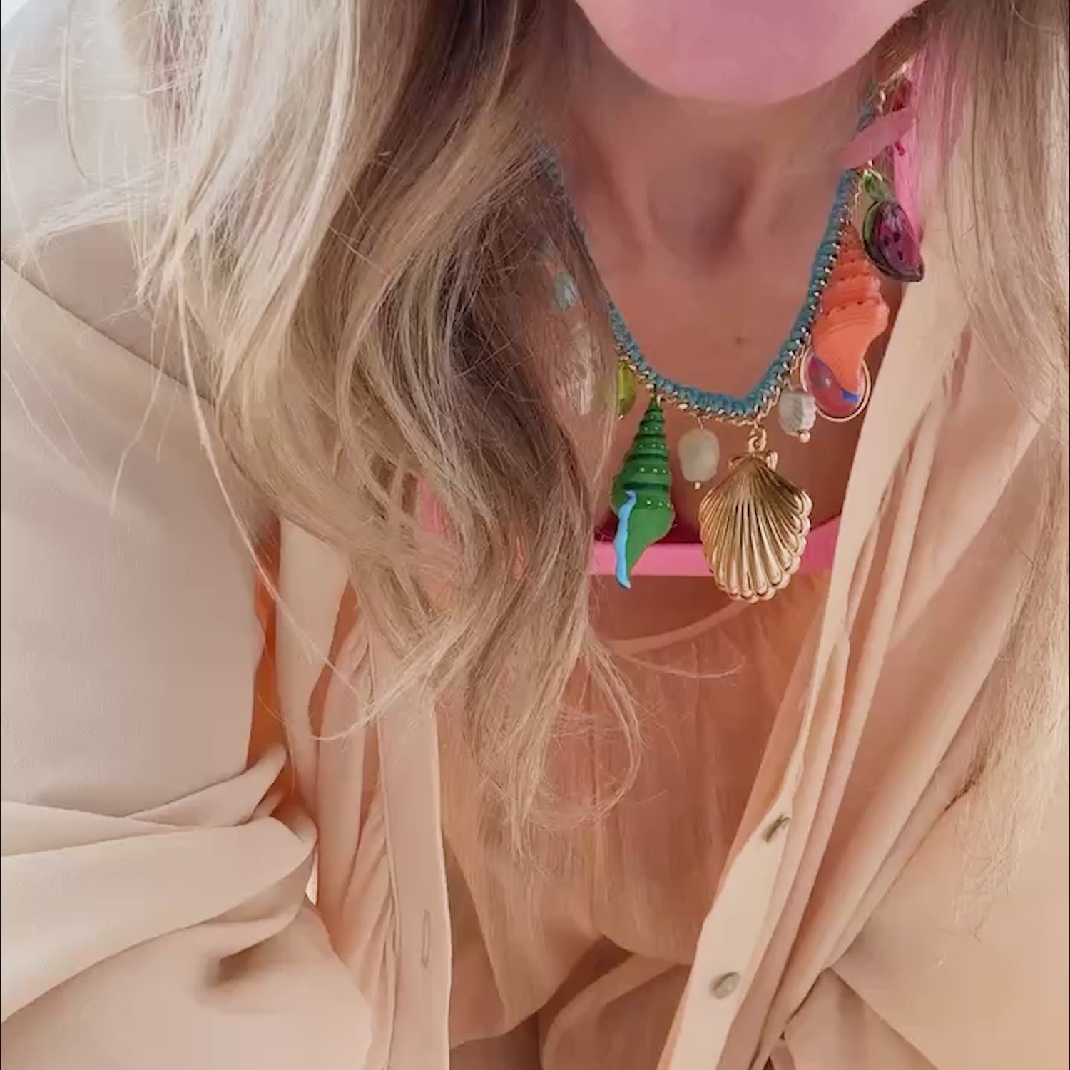Model wearing peach colored top with pink bandeau underneath. Showing off a shell and semi precious stone necklace around her neck with gold drop earrings on the streets of Merida, Mexico