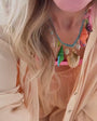 Model wearing peach colored top with pink bandeau underneath. Showing off a shell and semi precious stone necklace around her neck with gold drop earrings on the streets of Merida, Mexico