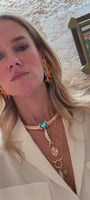 Model wearing orange beaded and embroidered earrings with a thick gold collar chain with bleu stone and fish pendant layered with gold necklaces